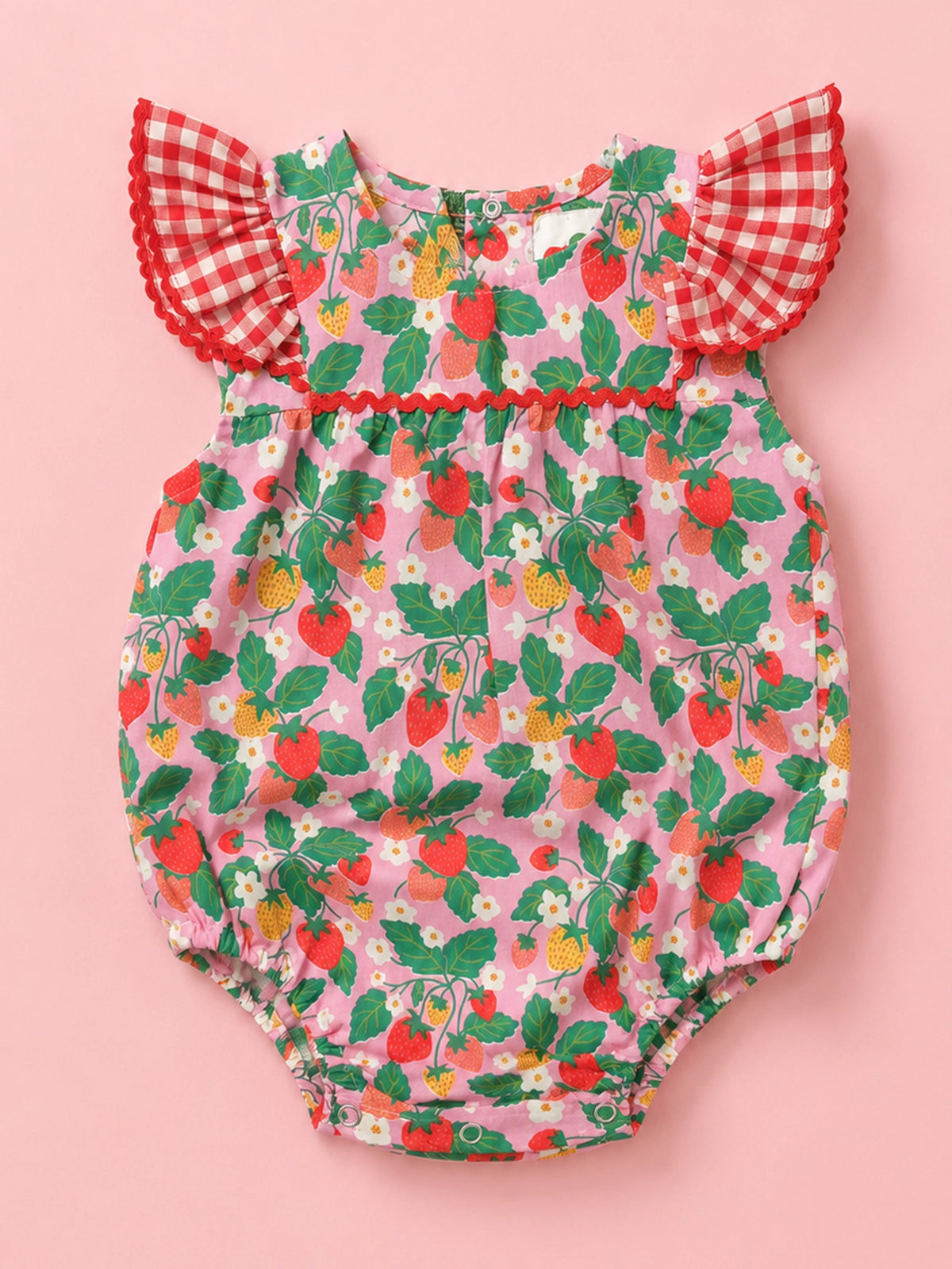A baby bubble romper with a pink strawberry and white flower print, featuring red and white gingham flutter sleeves with red pom-pom trim, laid flat on a solid pink background.