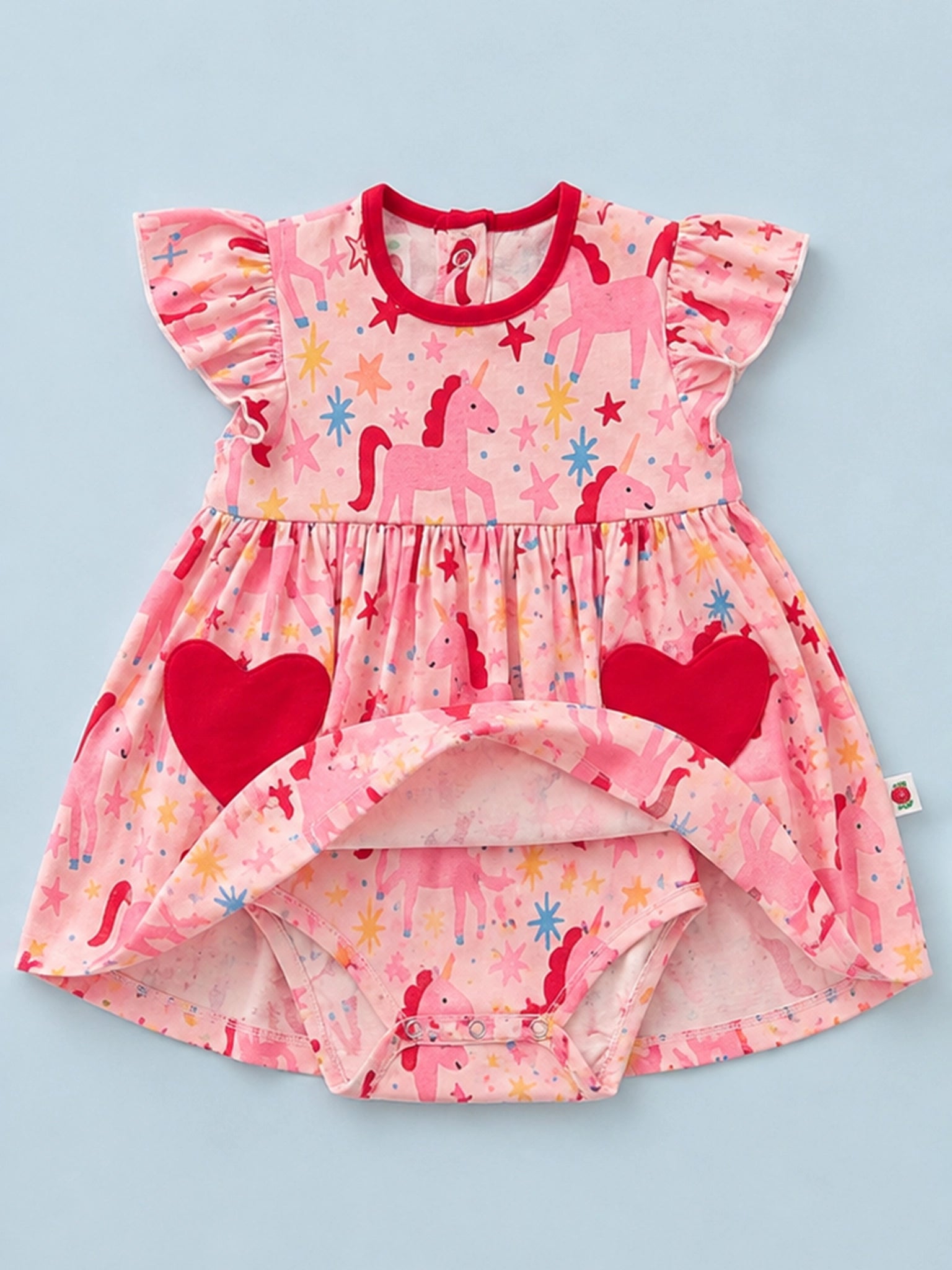 A baby girl's high-low dress with flutter sleeves, featuring a pink unicorn and star print, red heart pockets, and a red crew neck, laid flat on a light blue background.