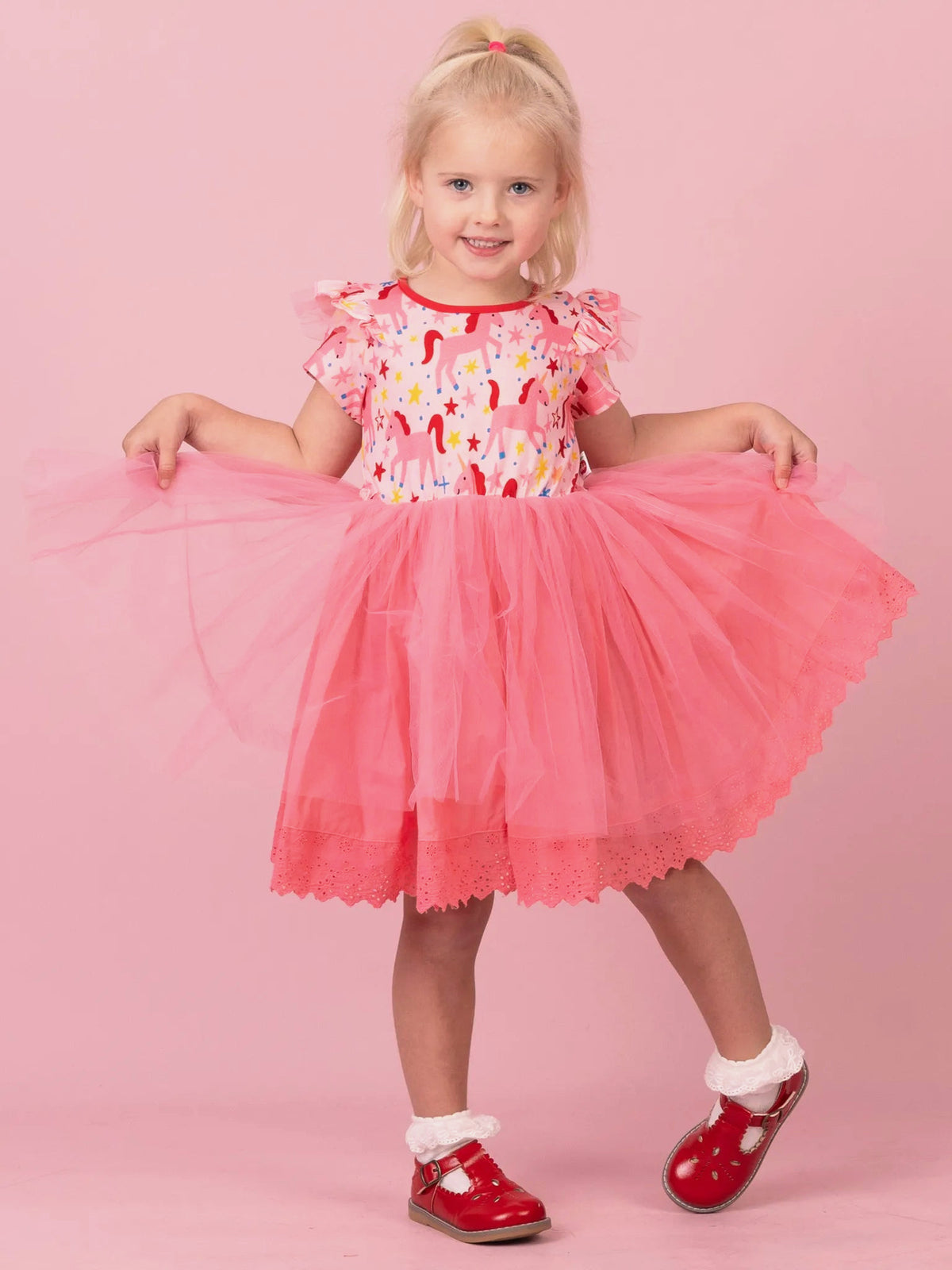 Girl holding out the pink tulle skirt of her Magical Unicorn tutu dress