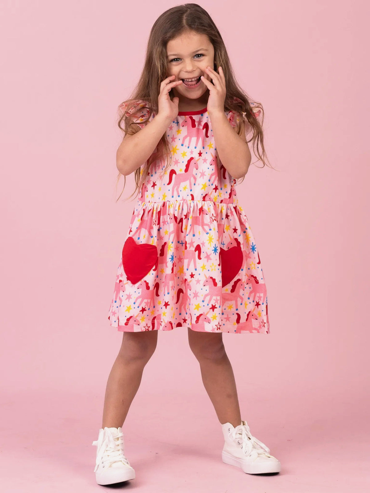 Girl giggling in pink Magical Unicorn skater dress with heart pockets