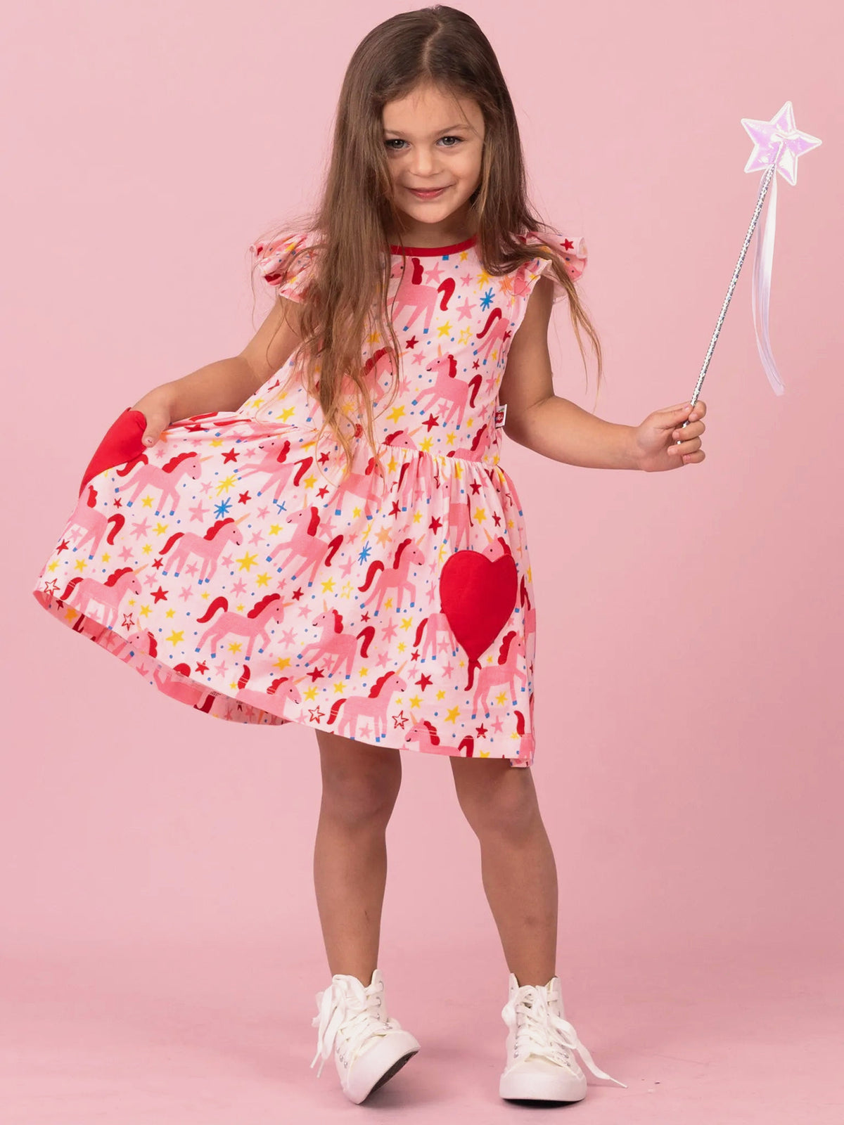 Girl twirling in Magical Unicorn skater dress with red heart pockets, holding a star wand
