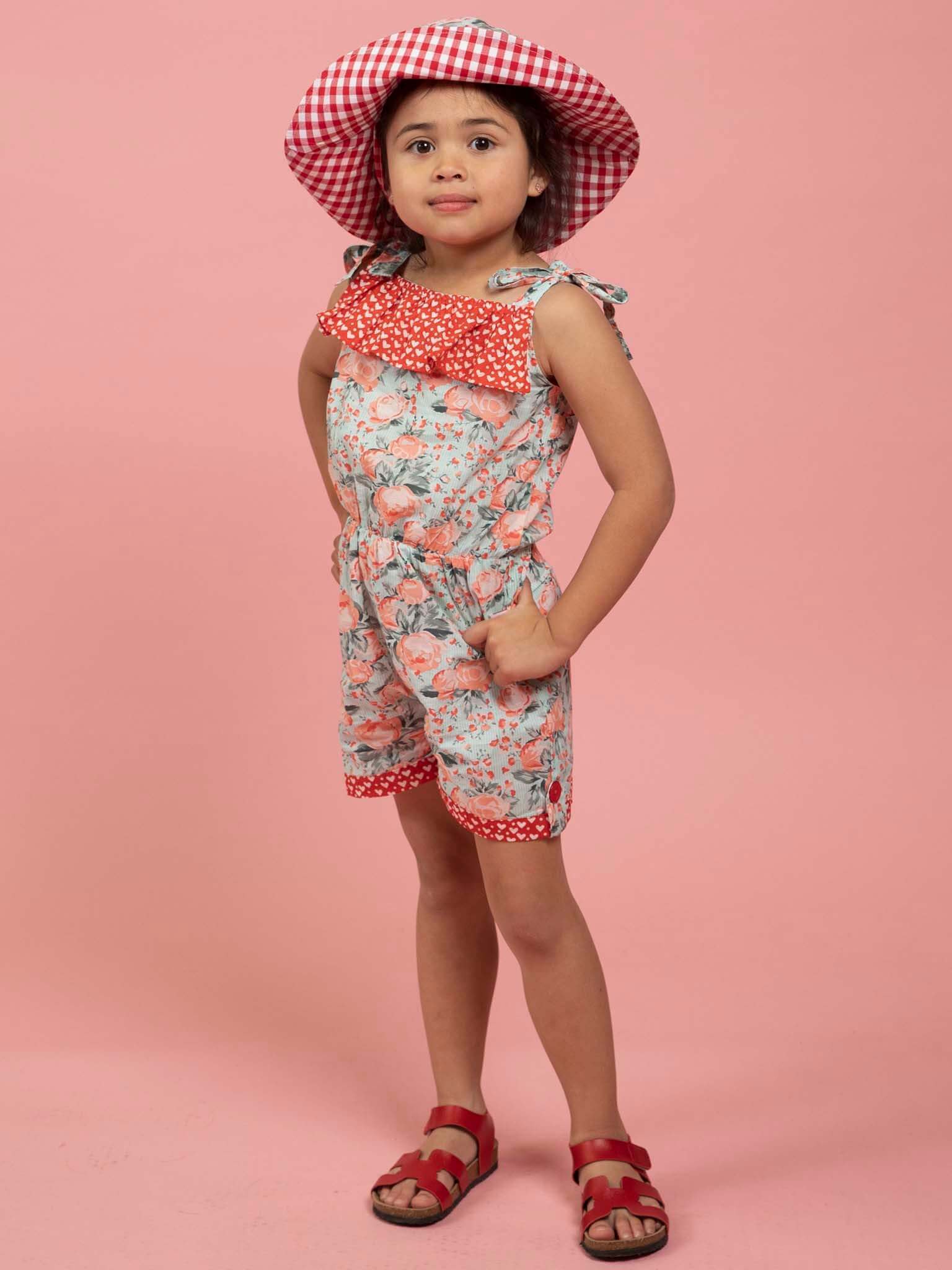 Young girl wearing a vintage roses floral romper and matching hat on a pink background