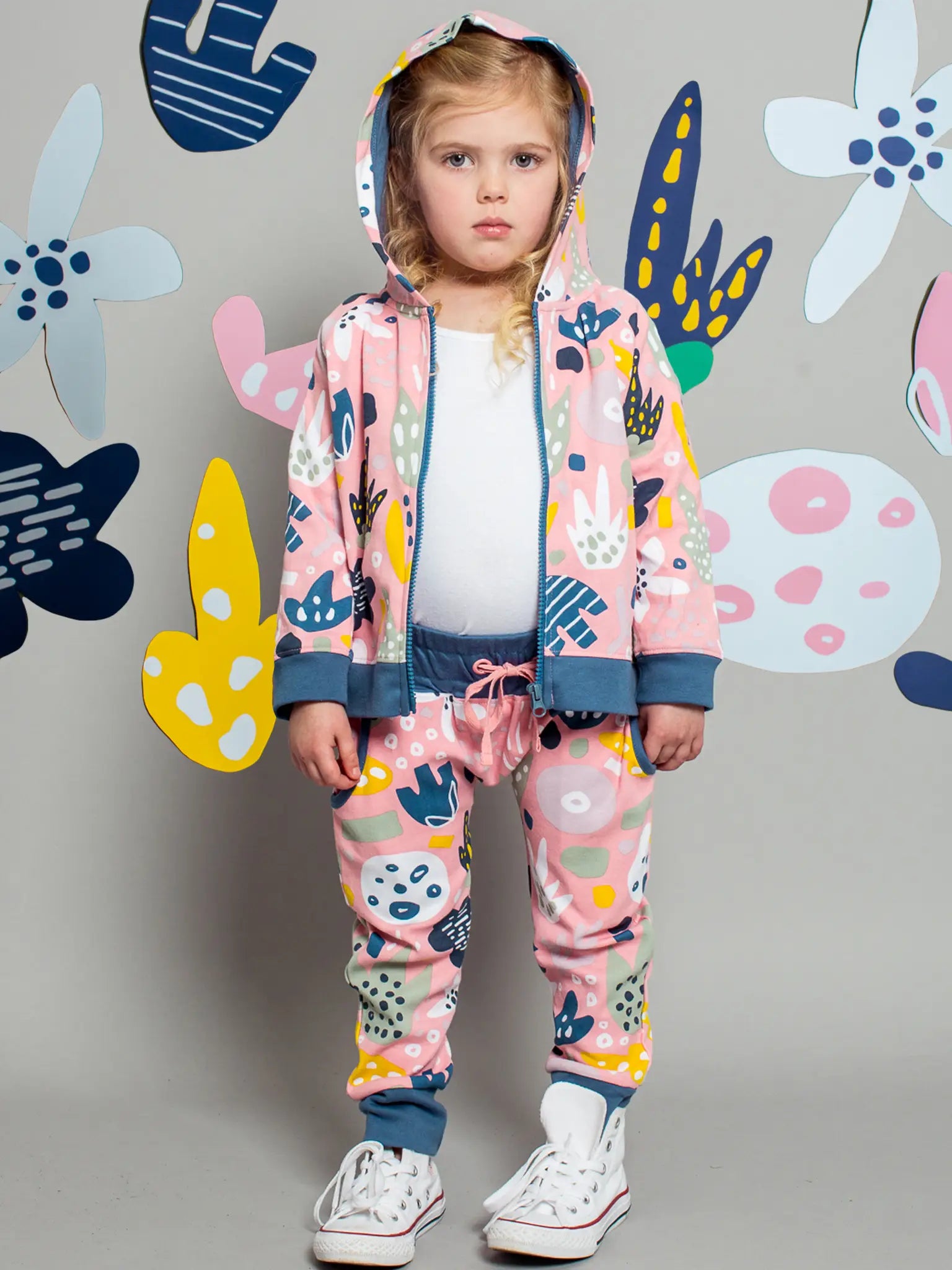 Child wearing a colorful outfit with floral patterns against a gray background with abstract shapes.