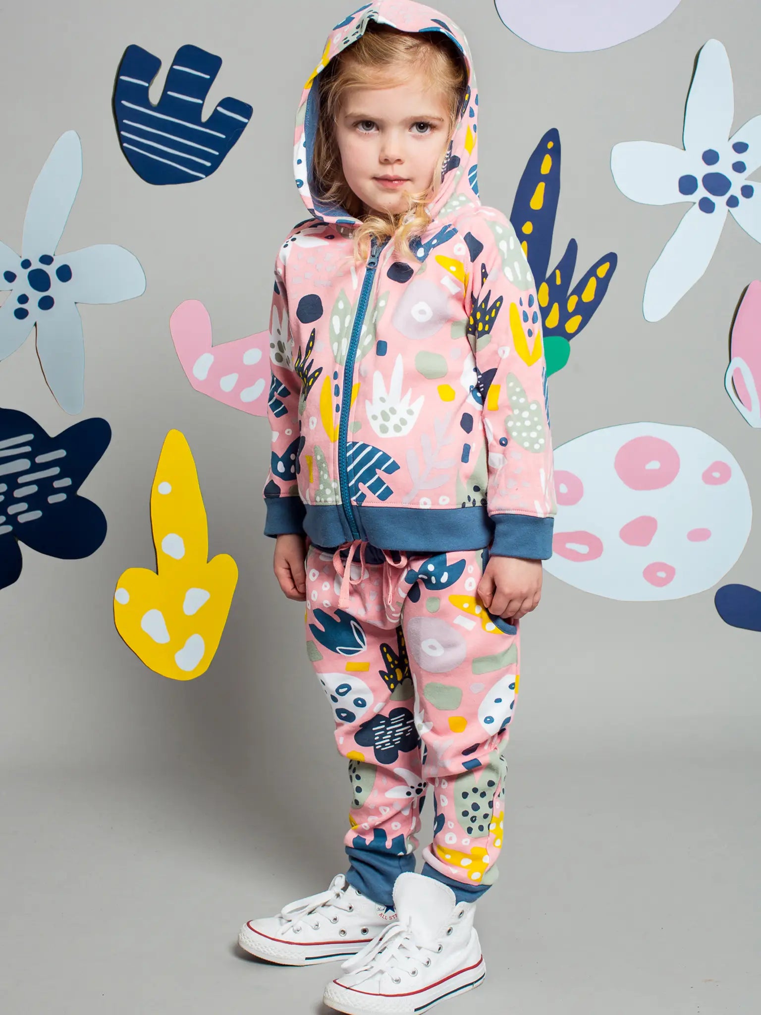 Child wearing a colorful tracksuit with abstract patterns against a gray background with decorative elements.