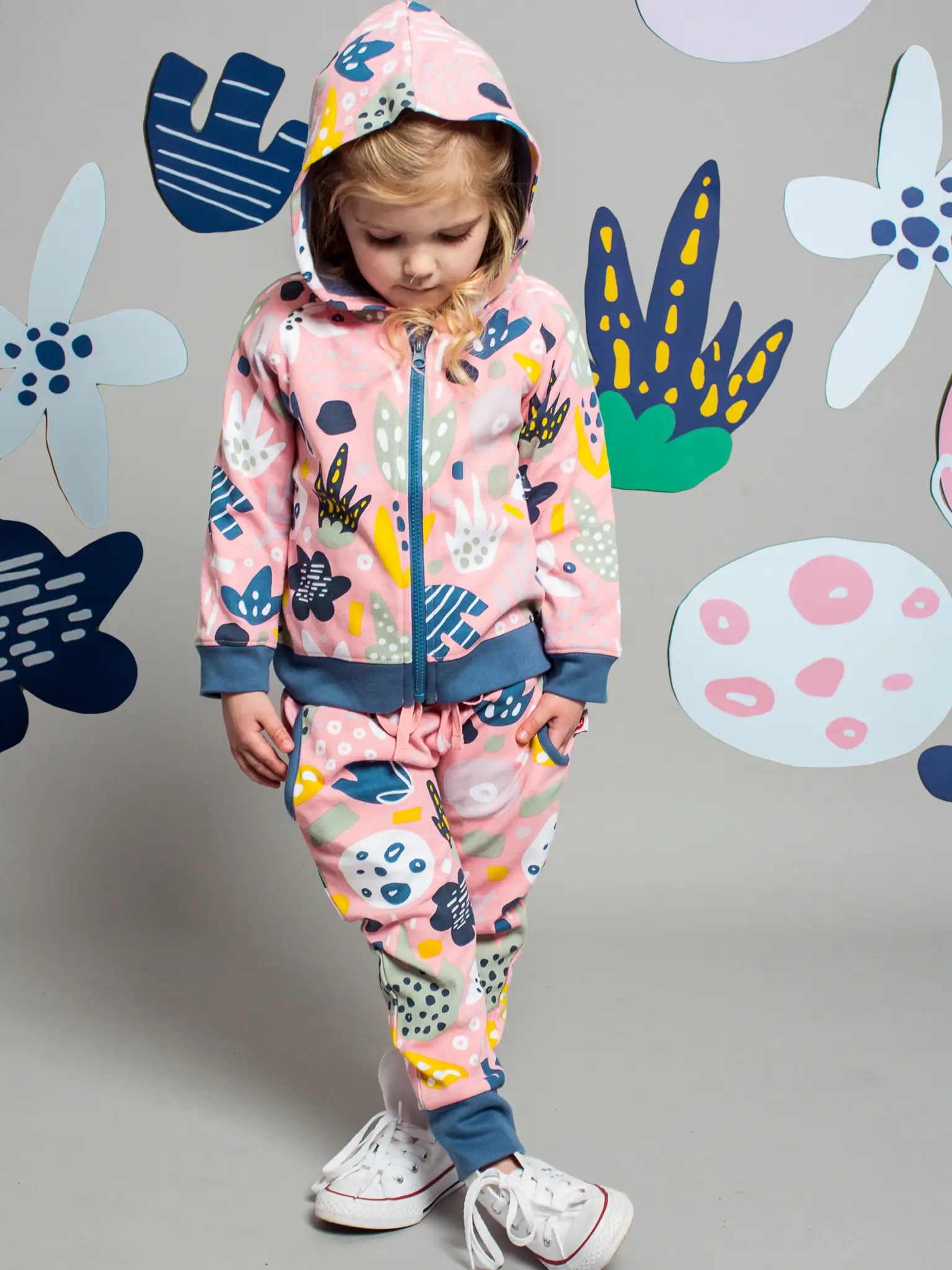 Child wearing a colorful outfit with a floral pattern against a gray background with abstract shapes.