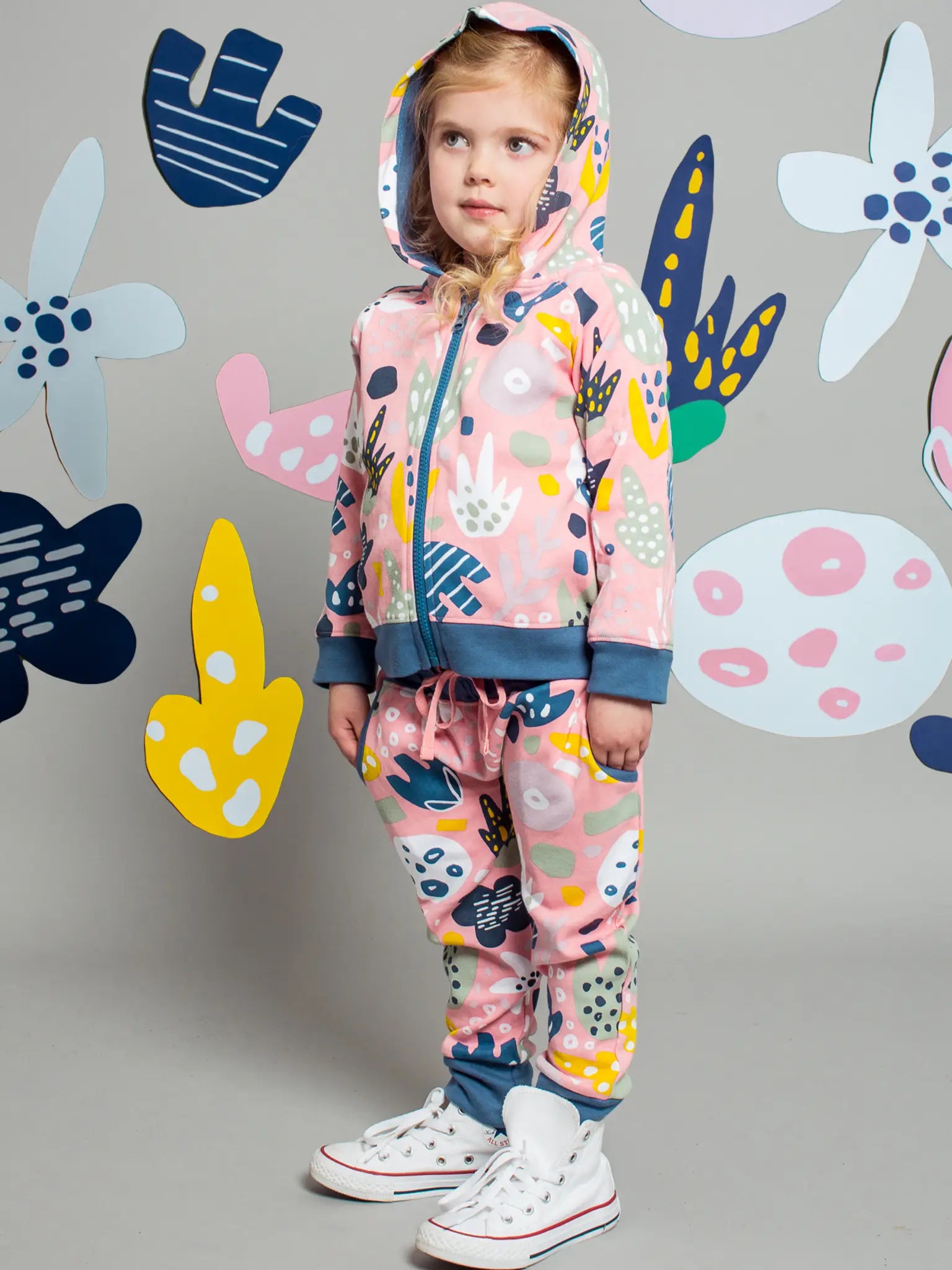 Child wearing a colorful outfit with abstract patterns against a gray background with decorative elements.