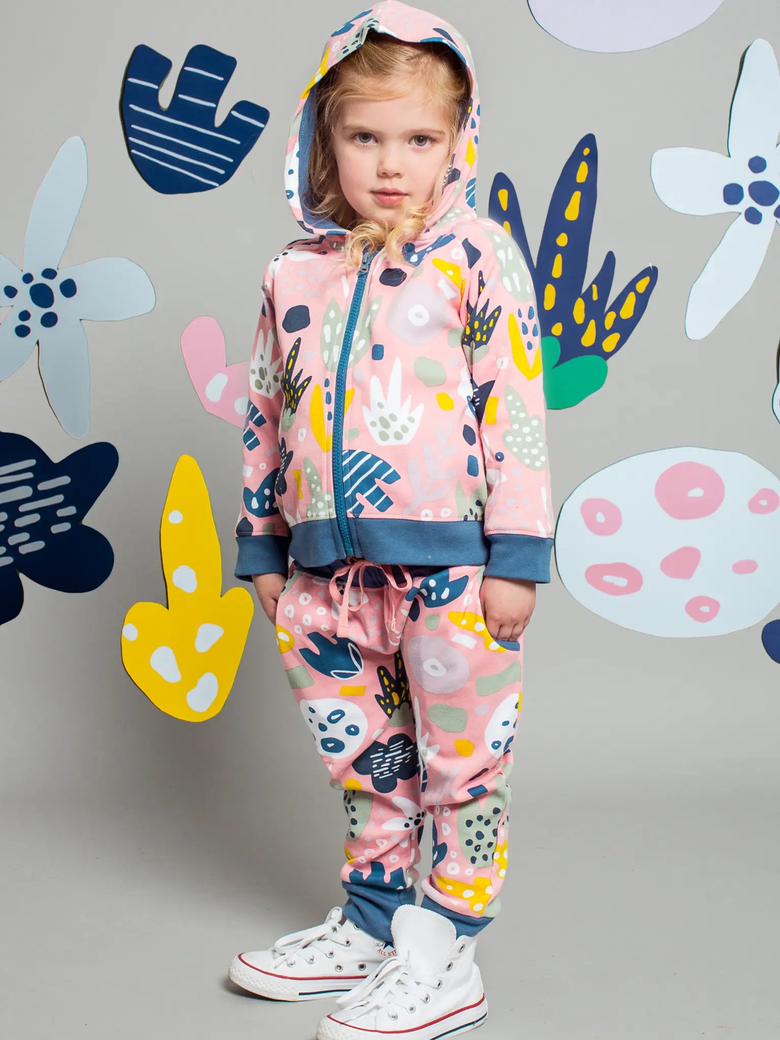 Child wearing a colorful outfit with abstract patterns against a gray background with abstract shapes.