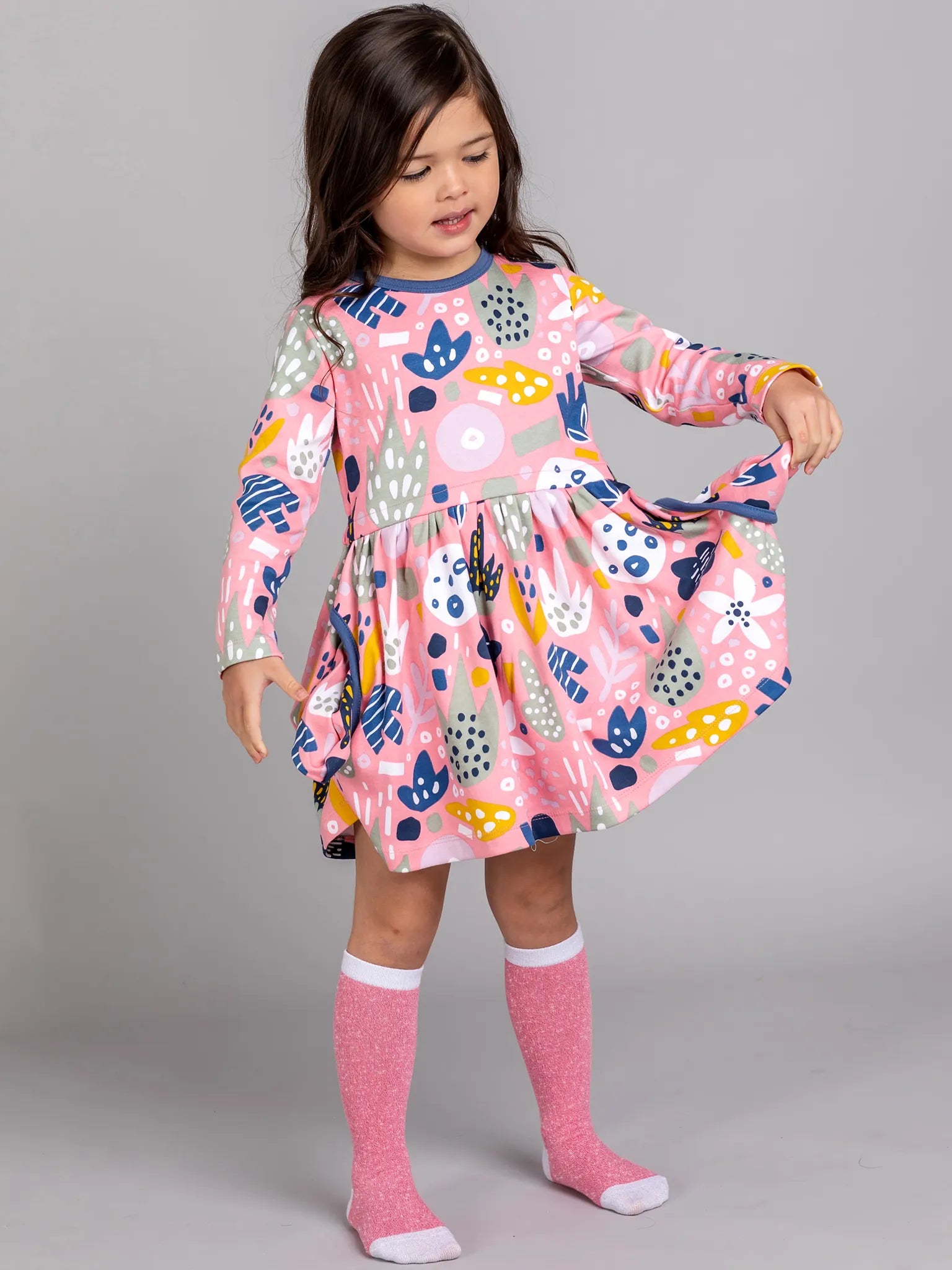 Young girl wearing a colorful dress with long sleeves on a gray background