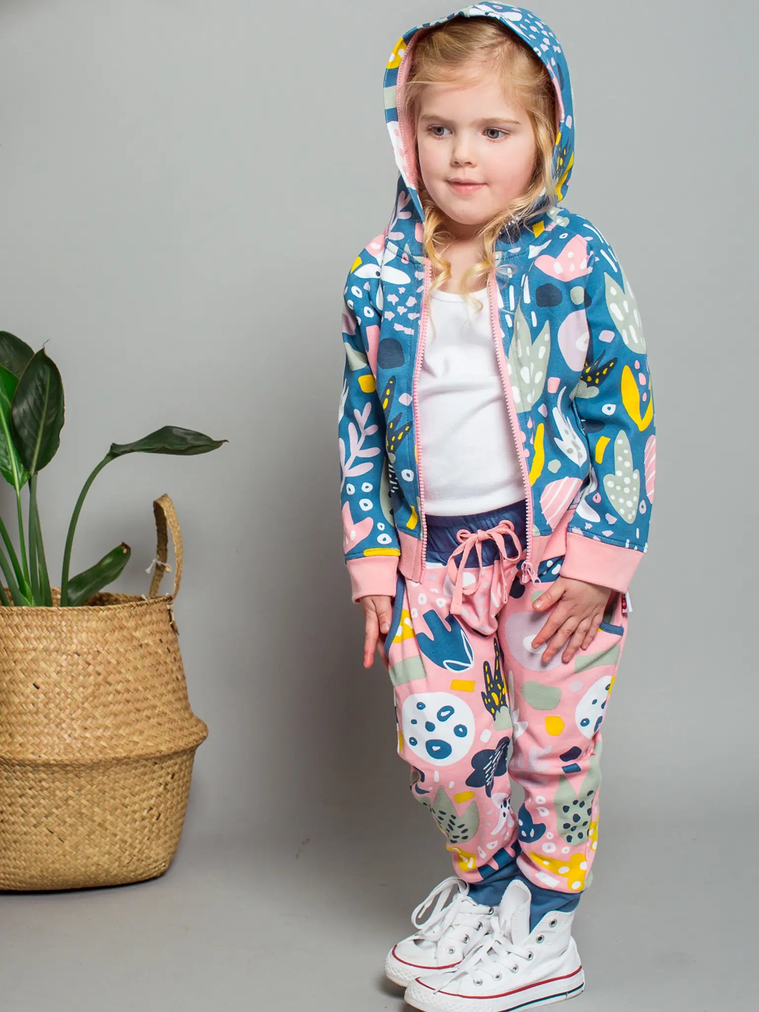 Child wearing a colorful animal-themed onesie with a plant in the background