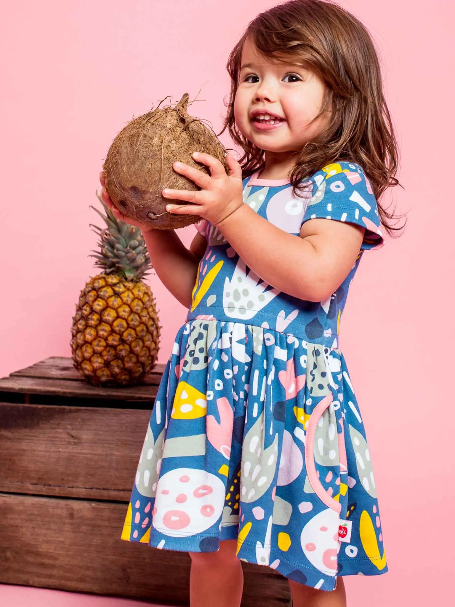 Smiling girl wearing a navy blue jungle print dress and holding a coconut