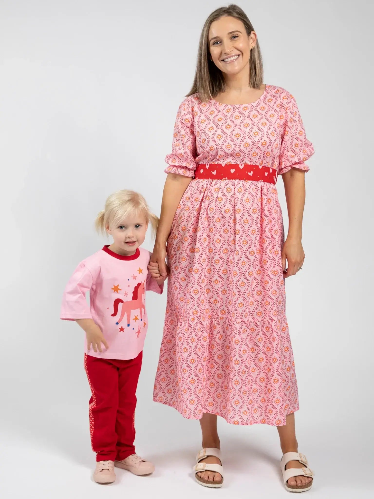 An adult woman in Blue Stripe's Women's Woodblock Maxi Dress stands beside a young girl in a pink shirt with a red unicorn and red pants, both facing the camera against a plain background.
