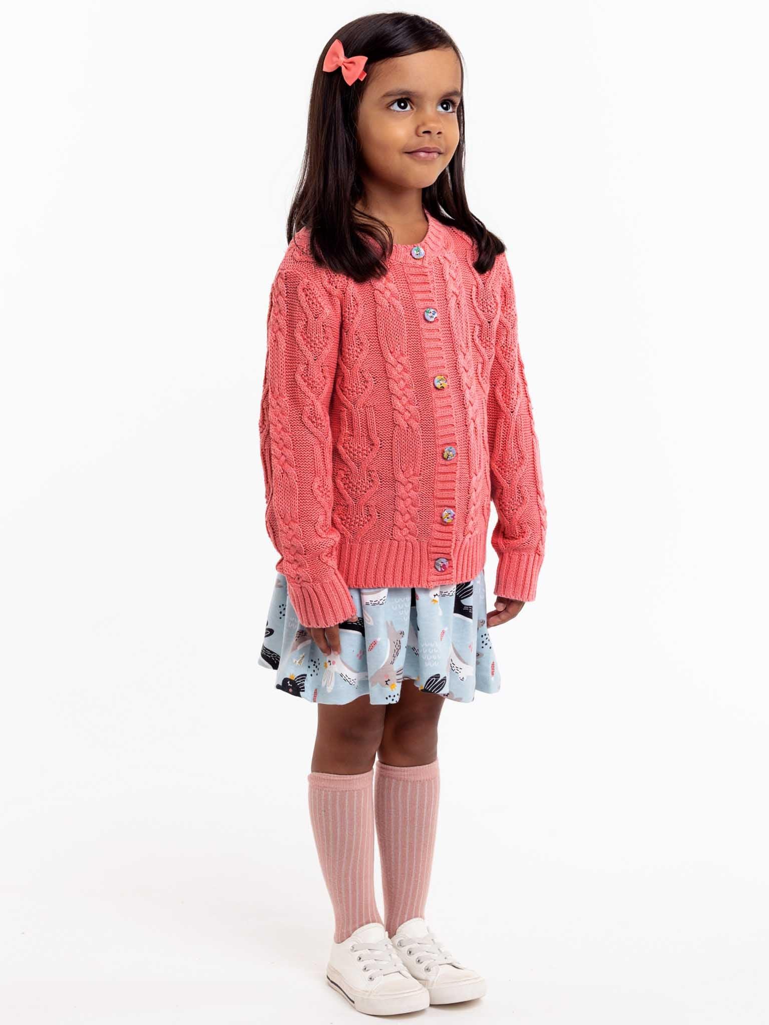 A little girl wearing a Willow Geranium Pink Cotton Cardigan by Knitwear with fabric covered buttons.