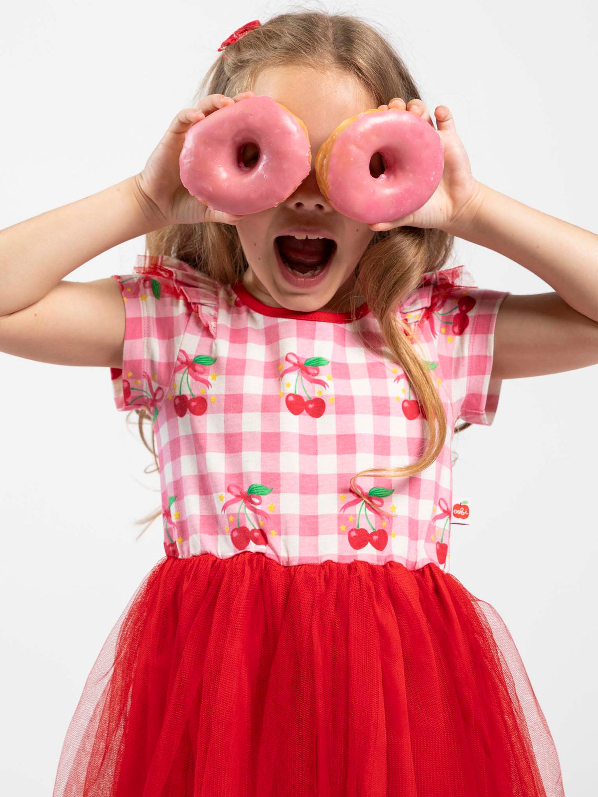 Girl in the Cherry Gingham Tutu Dress holding two pink doughnuts over her eyes