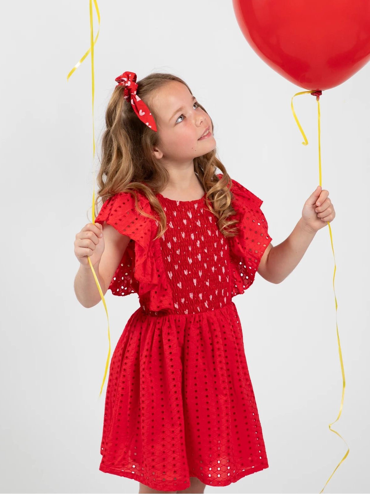 Young girl in a red dress holding pink and red balloons against a white background