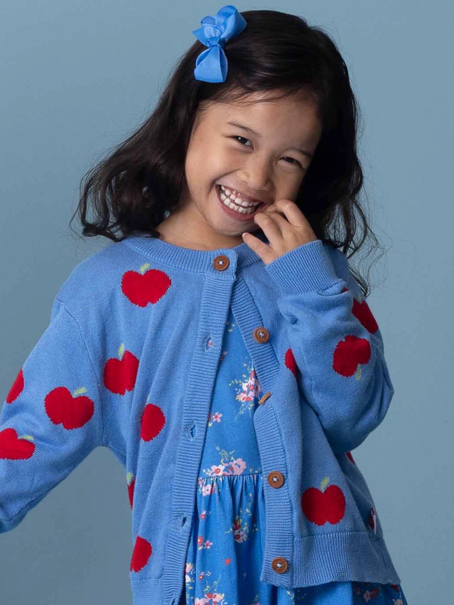 Young girl wearing a blue cardigan with red apple patterns on a gray background