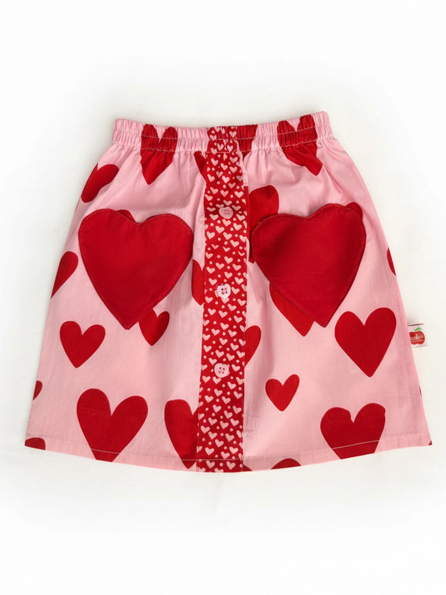 The Big Hearts Big Heart Pocket Skirt features red heart patterns, a central red panel with small white hearts, heart-shaped pockets, and an elastic waistband. Hand-printed cotton adds comfort and playful charm.