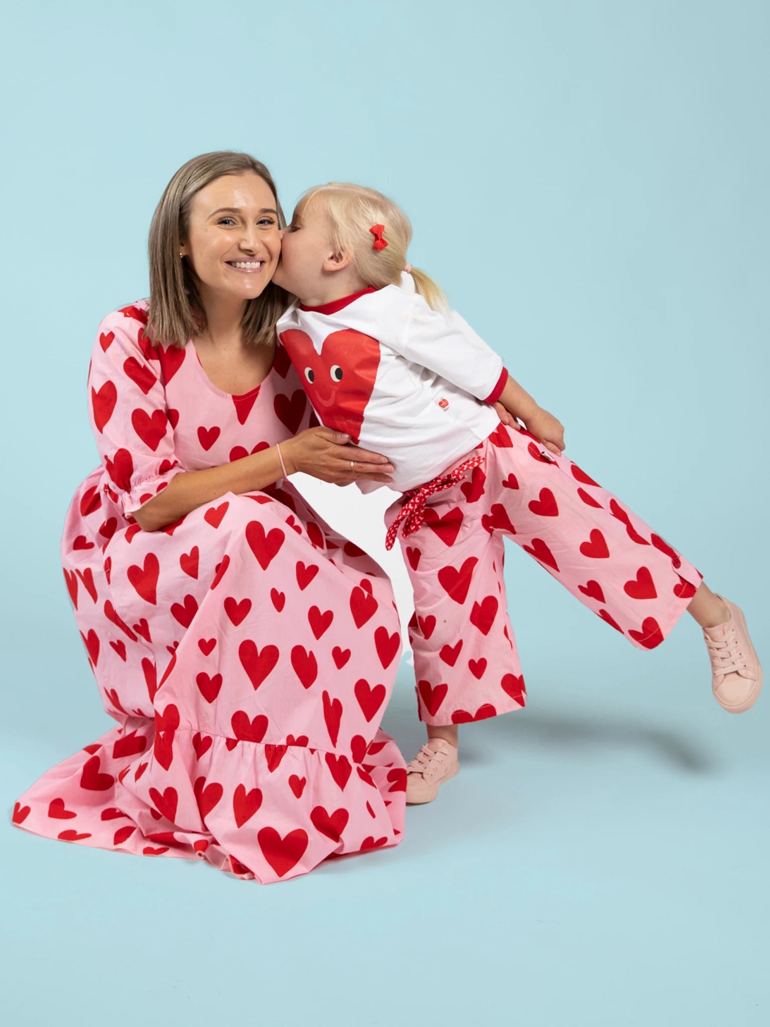 A woman and a young girl pose together in matching Big Hearts outfits, with the woman wearing the Women's Big Heart Maxi Dress; the girl kisses her cheek against a light blue background.
