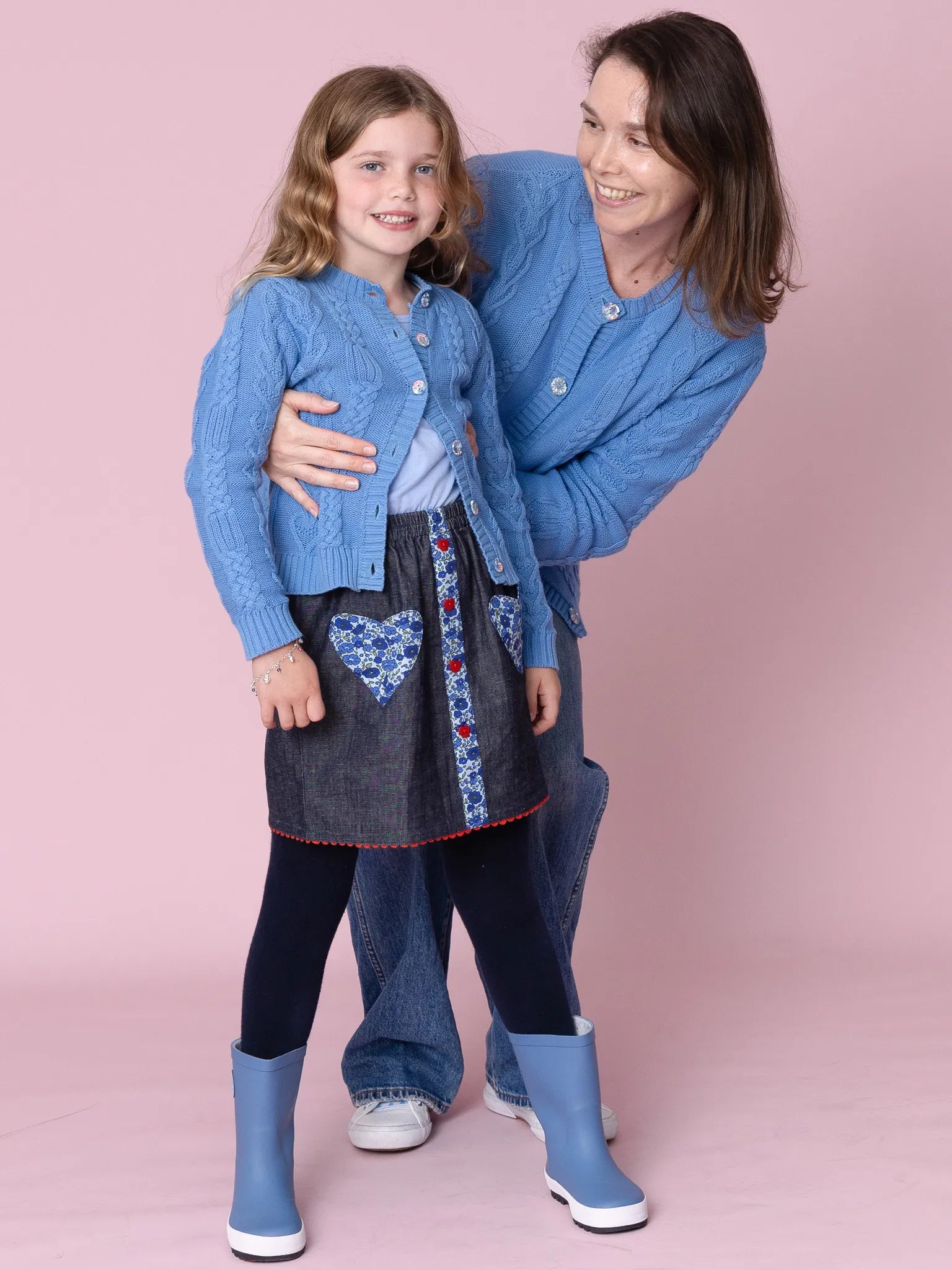 Woman and child wearing matching blue outfits with a pink background
