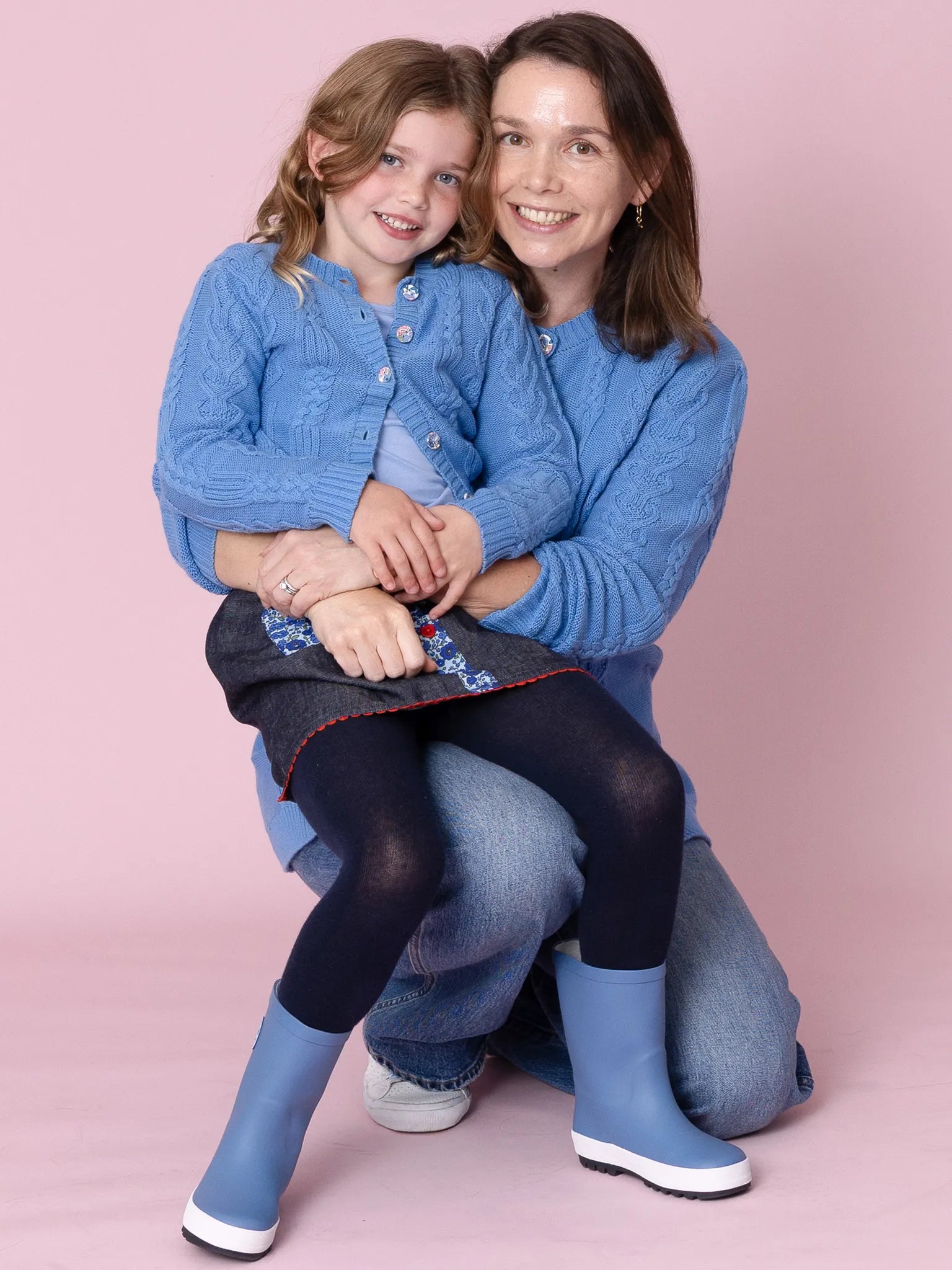 Woman and child wearing matching blue outfits against a pink background