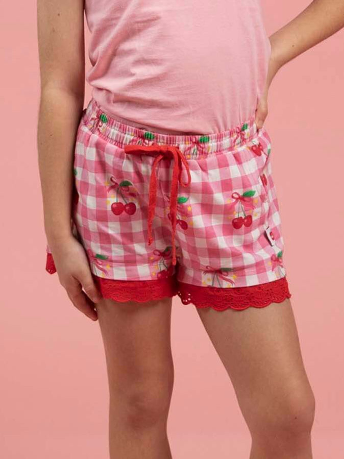 Young girl wearing a pink top and red checkered shorts on a pink background