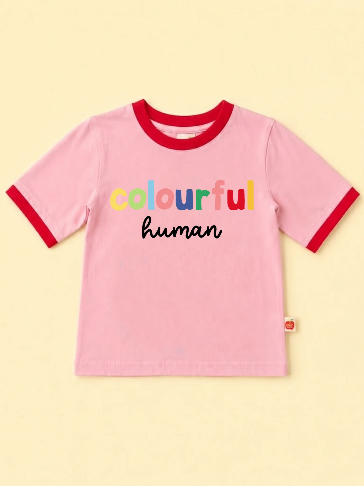 A pink ringer t-shirt with red trim on the collar and sleeve cuffs, featuring the text 'colourful human' printed on the chest. The word 'colourful' is written in a playful multicolor font, and 'human' is in black cursive script.