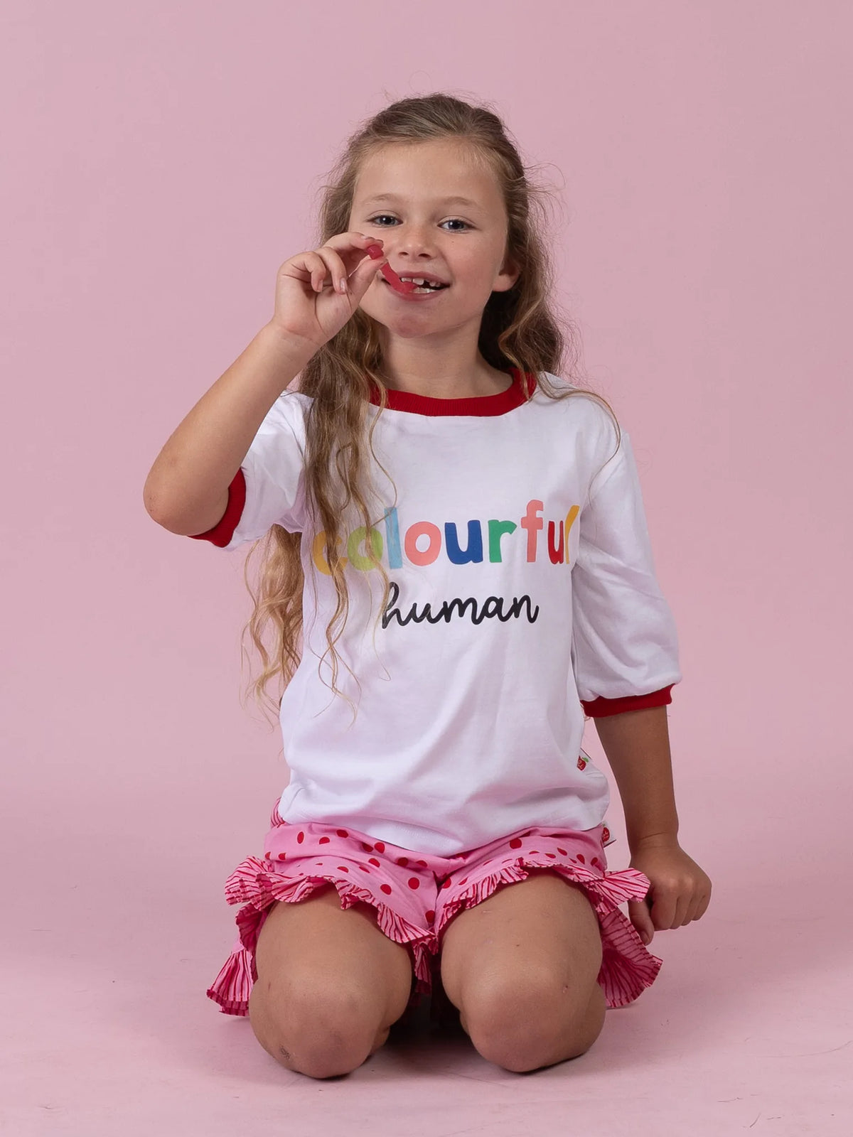 Girl kneeling in the white Colourful Human tee and Pink & Red Dots ruffle shorts