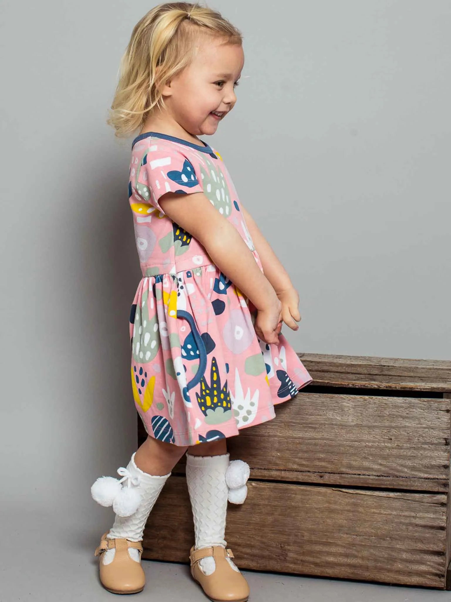 Smiling girl wearing a pink jungle print dress and white pom pom socks