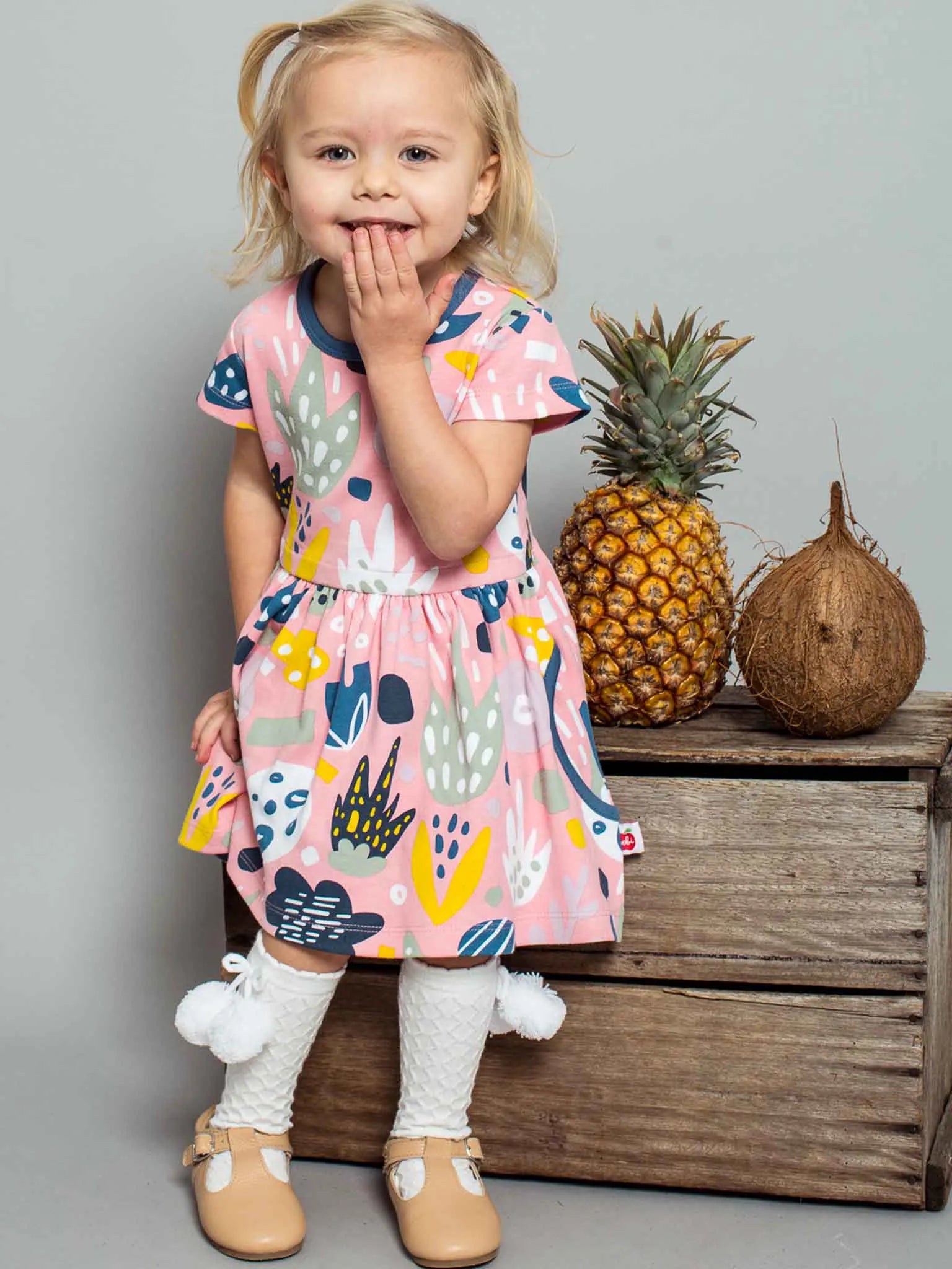 Smiling girl wearing a pink jungle print dress and white pom pom socks