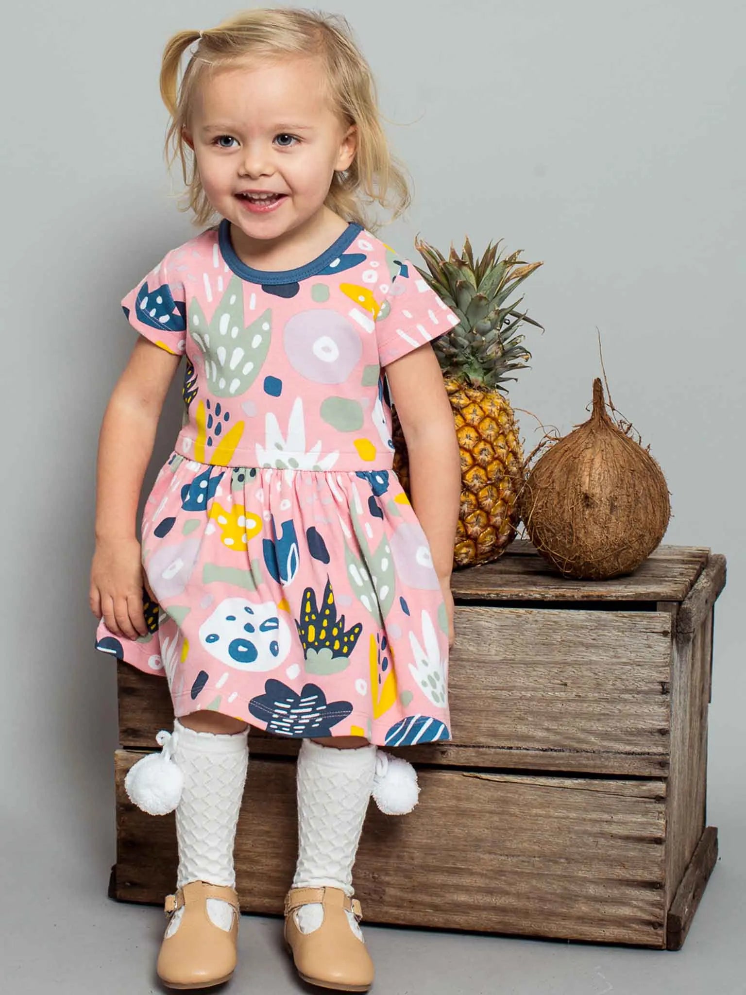 Smiling girl wearing a pink jungle print dress and white pom pom socks