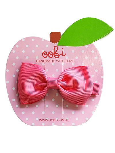 A pink Geranium Large Bow on a pink, apple-shaped card labeled "oobi handmade with love" with a green leaf accent by Essentials.
