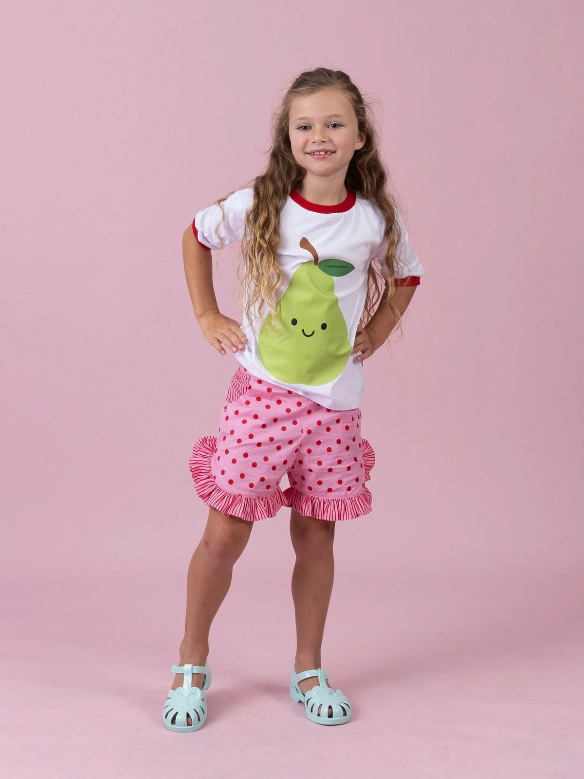 Girl in the white Happy Pear tee and Pink & Red Dots ruffle shorts, hands on hips