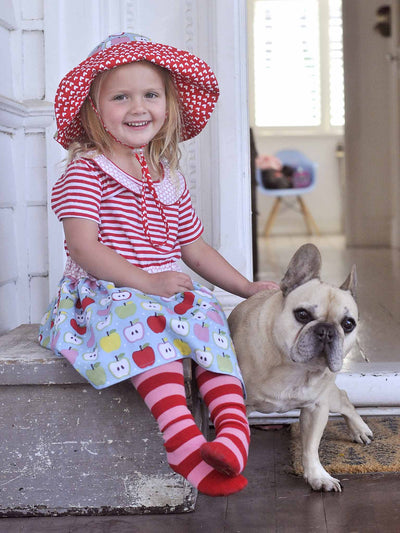 A girl sitting on a step next to her dog, wearing an Oobi Free MYSTERY Hat.