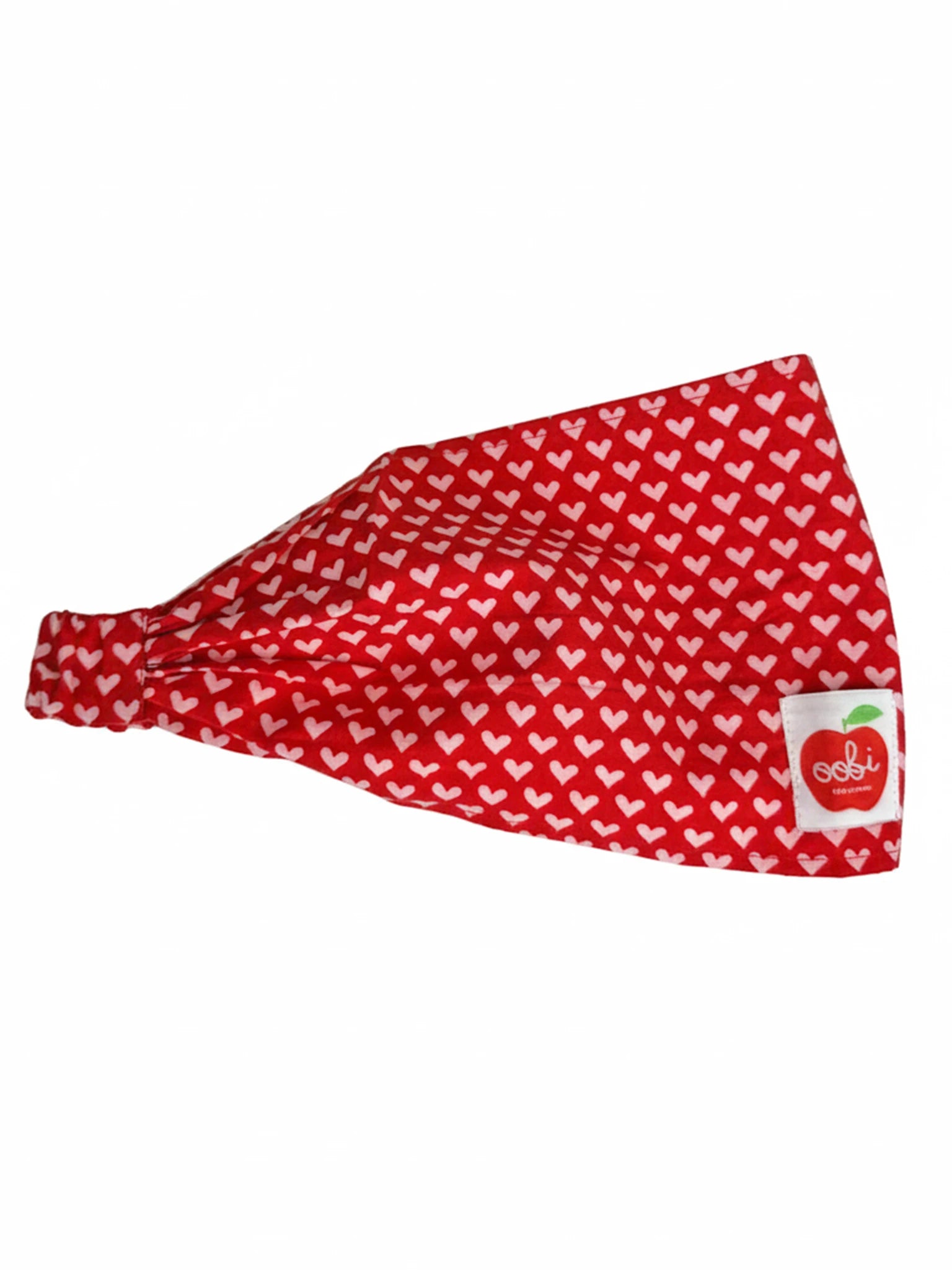 The Essentials Red and Pink Hearts Headband features an oversized red fabric design with small white and pink heart patterns, plus a sewn-on label showing a red apple and the brand name "ooki.