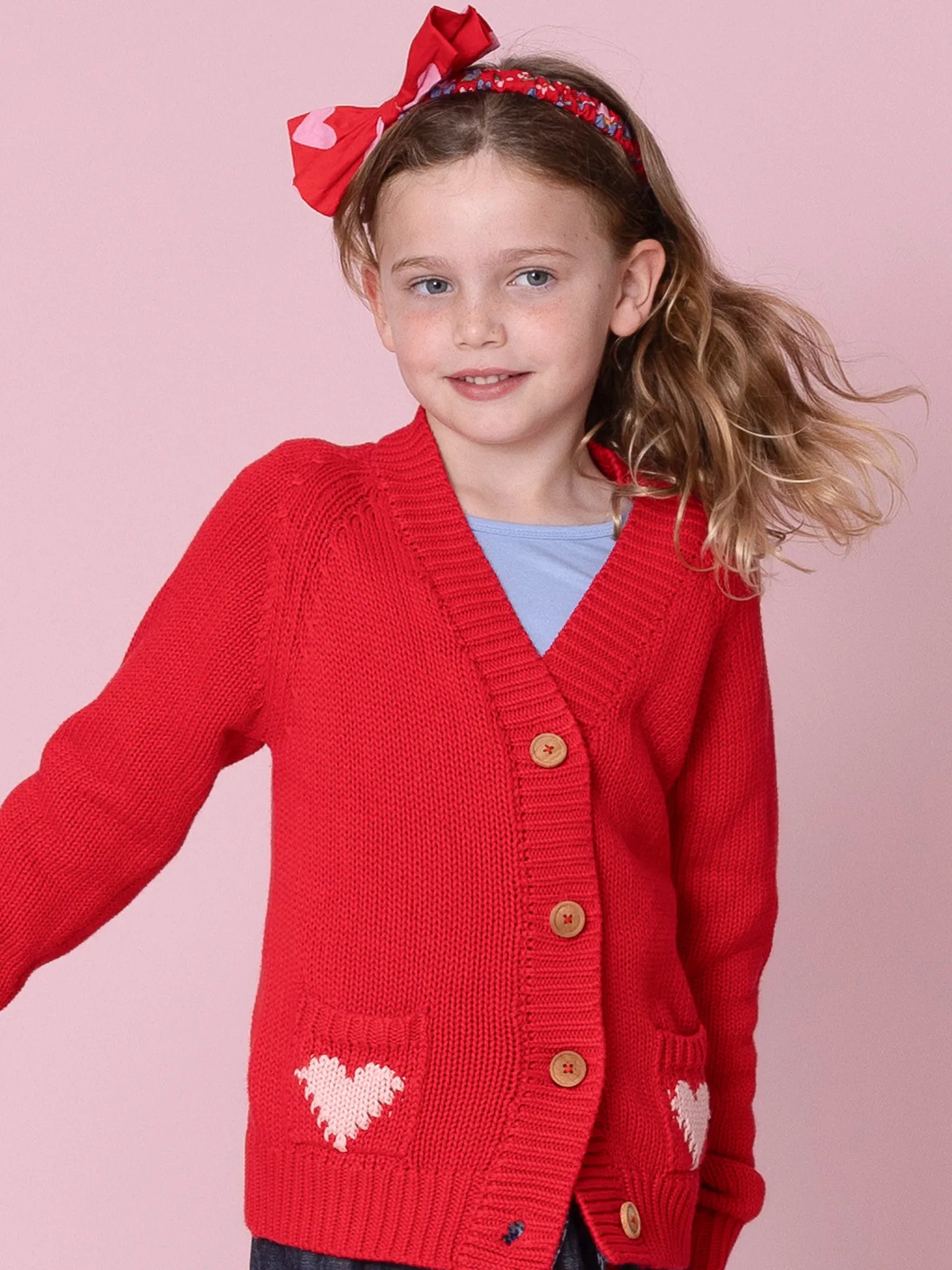 Young girl wearing a red cardigan with heart designs on a pink background