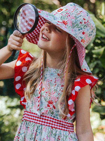 Young girl looking through a magnifying glass while wearing a floral patterned dress and an adjustable Bunny Chloe Hat with a wide brim.