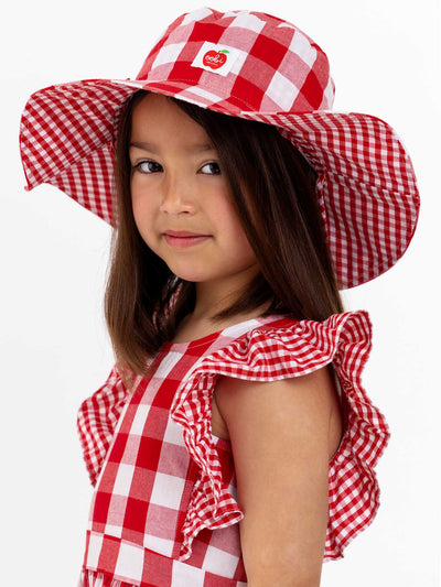 A little girl wearing a Red Check Chloe Hat dress and hat with a brim.