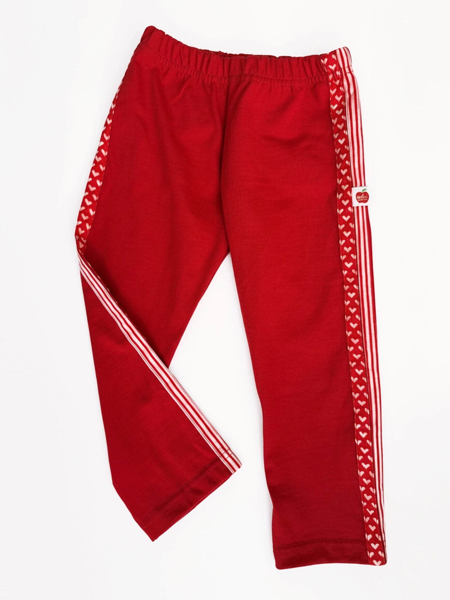 The Essentials Red Jersey 2 Stripe Pants feature white stripes and heart patterns along the side seams, ideal for girls’ sportswear. Shown laid flat on a white background.