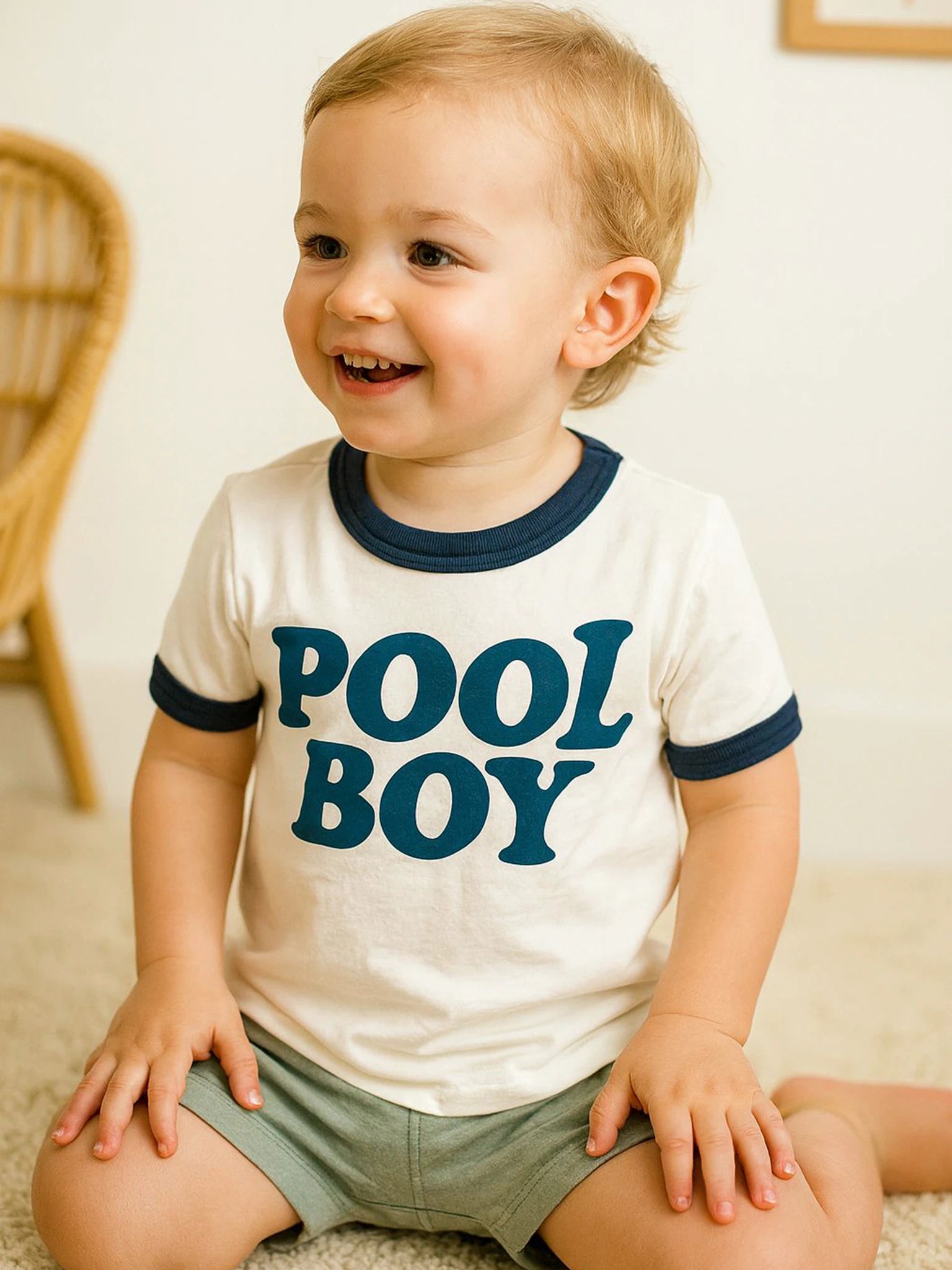 A happy toddler sits indoors wearing the Oobi Pool Boy Tee with Navy Binding, featuring bold lettering—one of our favorite boys' tees, hand printed in Australia.