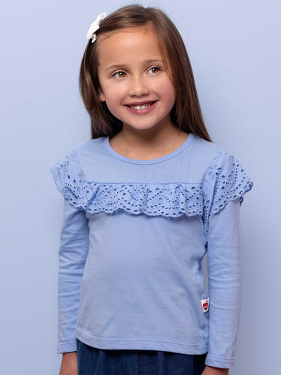 Young girl with a white hair clip, smiling, wearing an Essentials Lace Front Tee Blue - Imperfect with lace detail on a soft purple background.