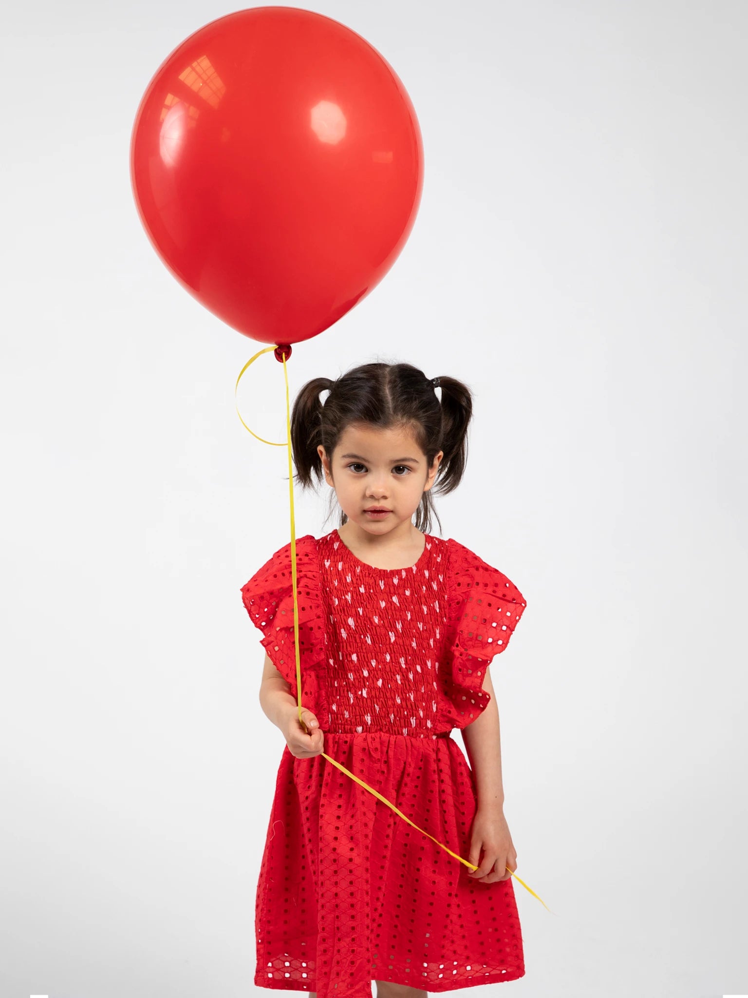 Young girl in a red dress holding a red balloon against a white background