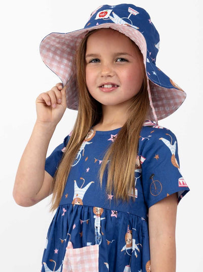 A little girl named Chloe, dressed in a blue summer dress and wearing a Navy Circus Chloe Hat.