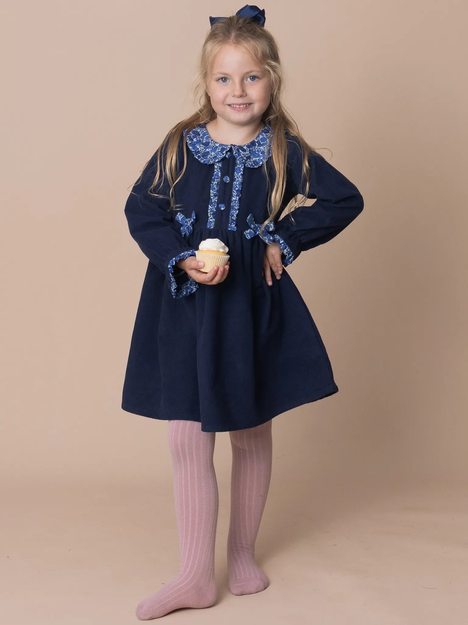 Young girl wearing a navy dress with blue embroidery against a beige background