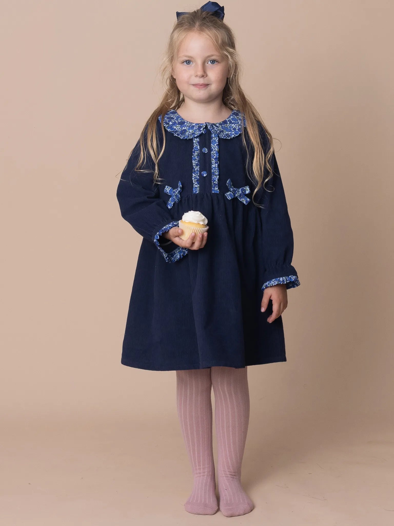 Young girl wearing a navy dress with floral embroidery on a beige background