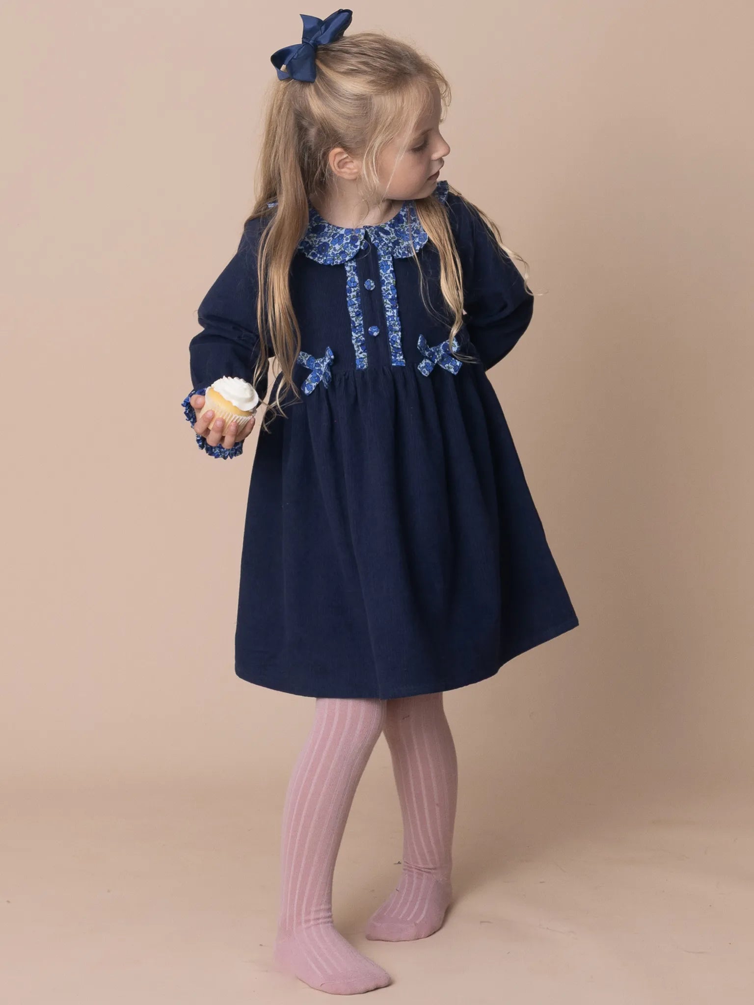 Young girl wearing a navy dress with lace details on a beige background
