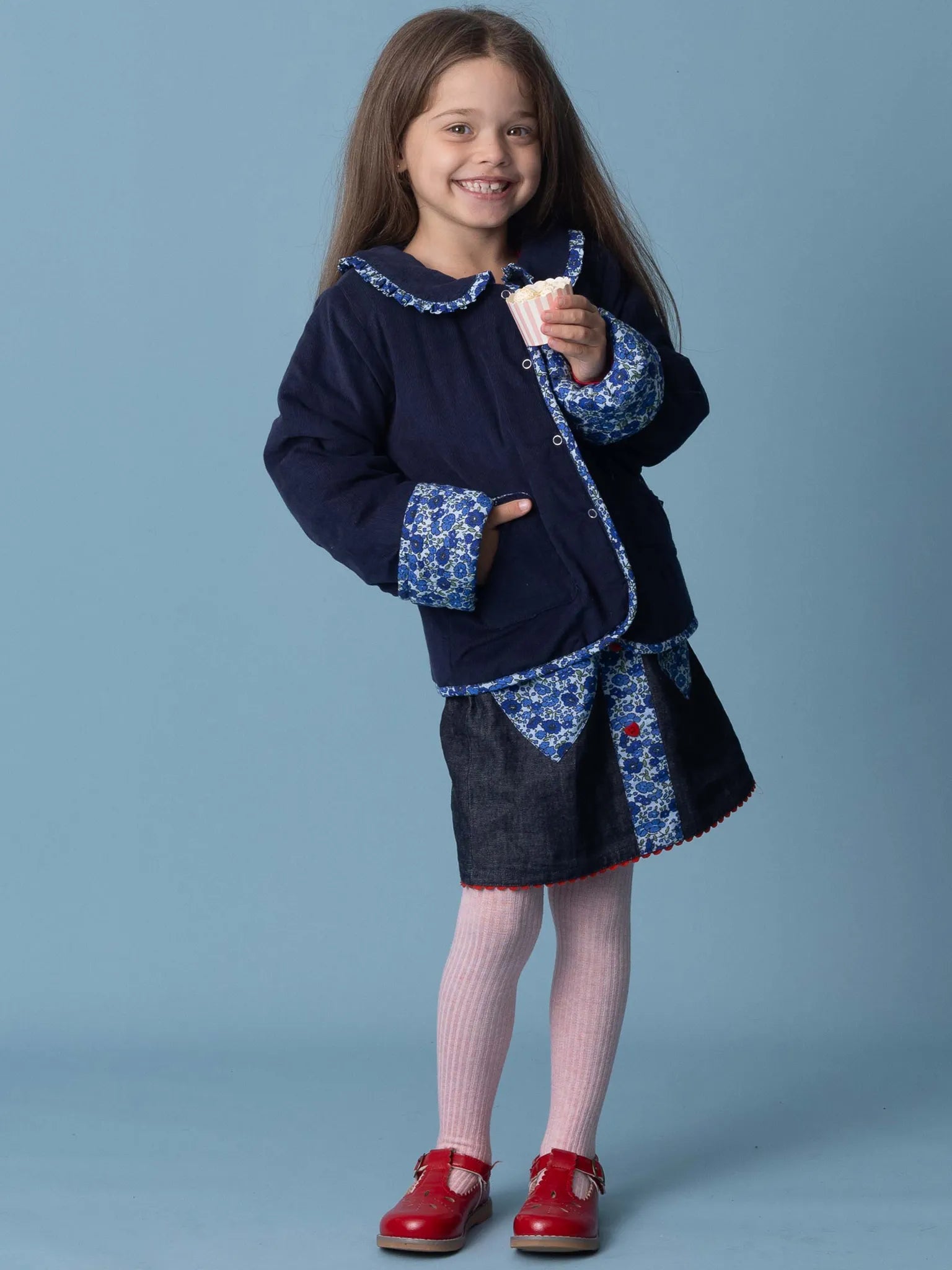 Young girl wearing a navy blue dress with floral patterns against a light blue background