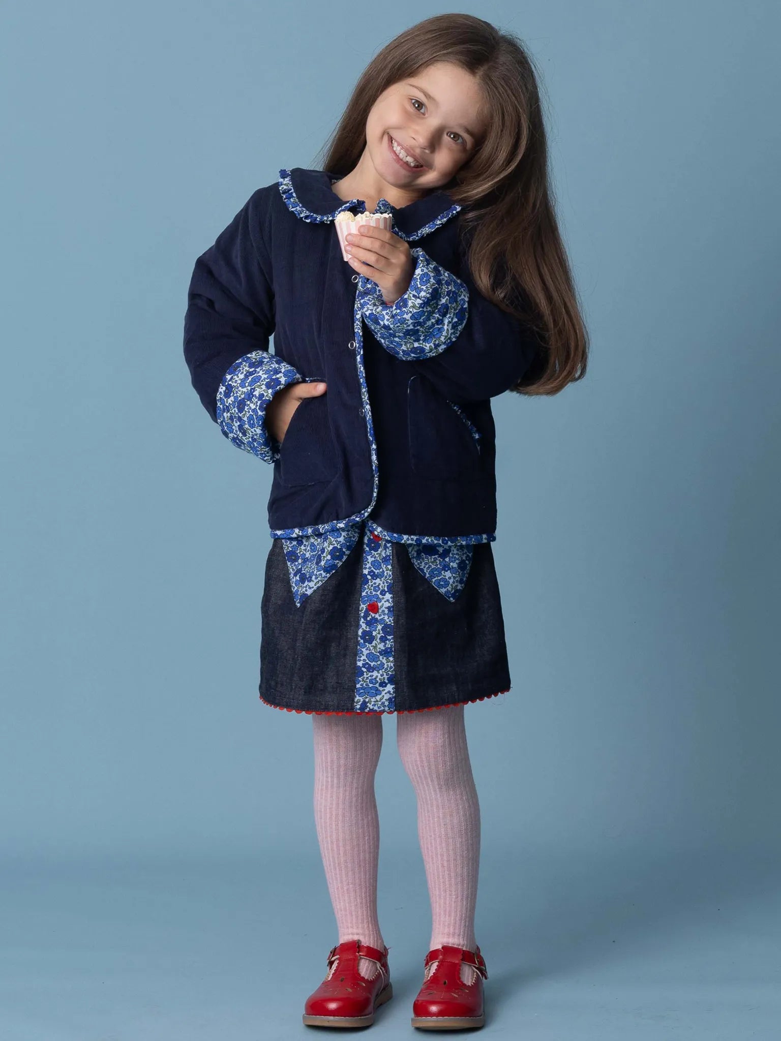 Young girl wearing a navy coat with floral patterns on a blue background
