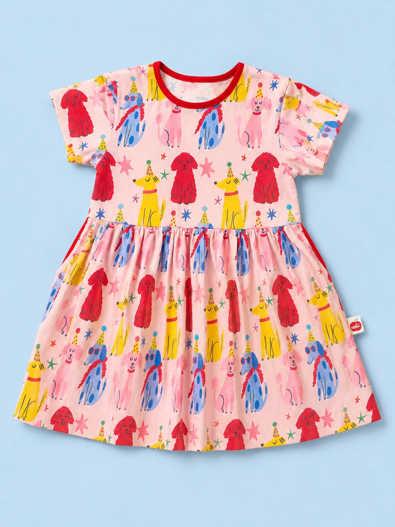 A short-sleeve baby dress with a pink base and a colorful print of party-dressed dogs, stars, and stripes, shown flat on a light blue background.