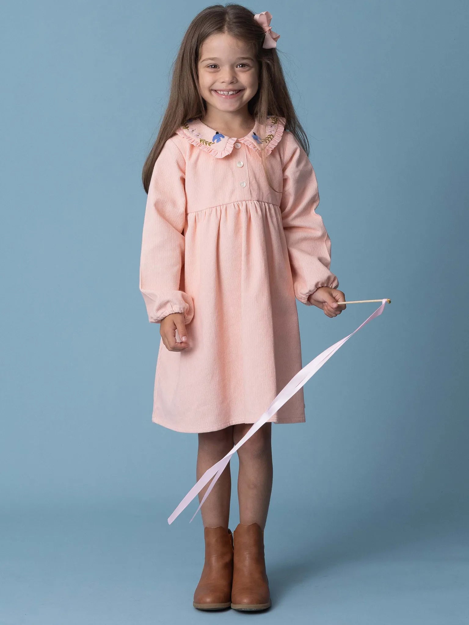 Young girl in a pink dress holding a ribbon against a blue background
