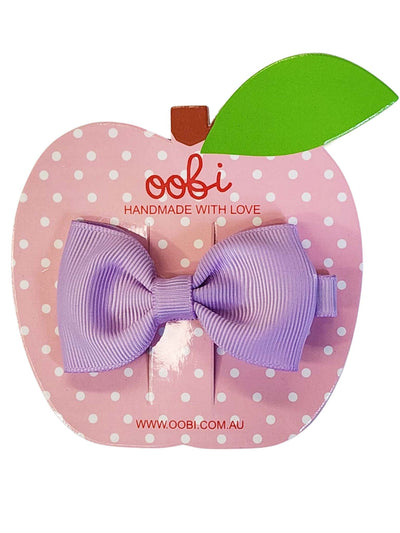 Pink apple-shaped card with white dots displaying a Violet Large Bow clip from Essentials, labeled "oobi handmade with love," with a green leaf and website address.