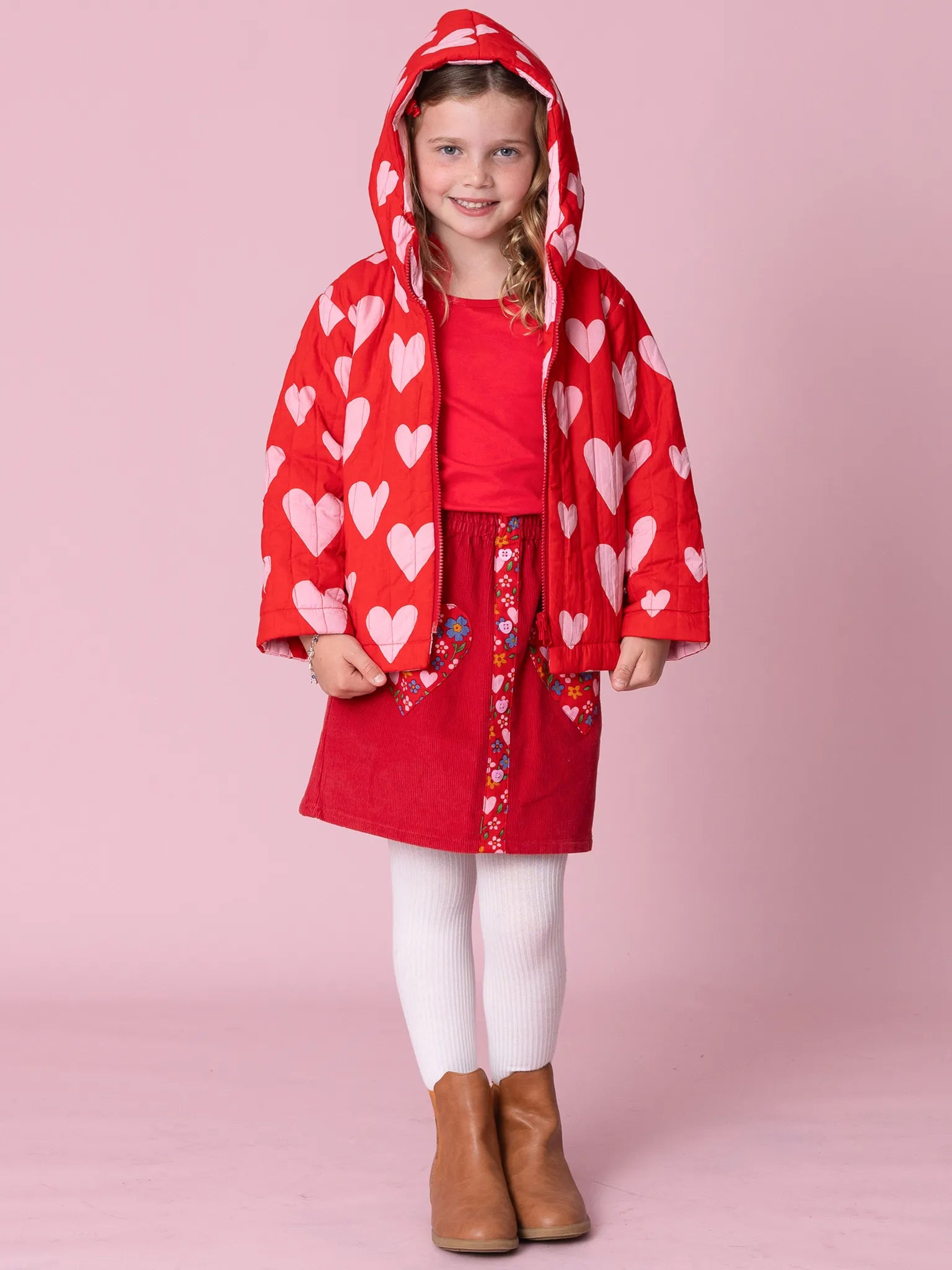 Young girl wearing a red heart-patterned raincoat against a pink background